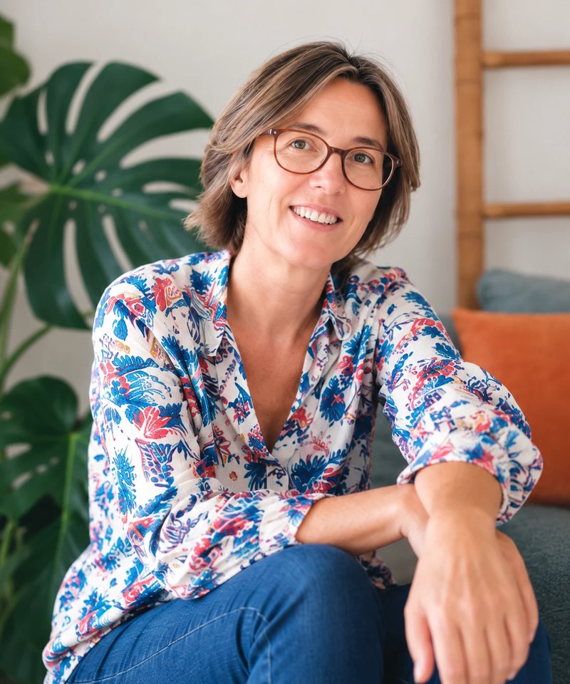 Marie-Noëlle, souriante, assise devant une plante verte